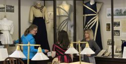 Three women in front of historic clothing exhibit.