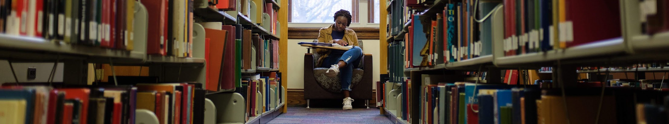 Photo of student studying at the end of a long row of books