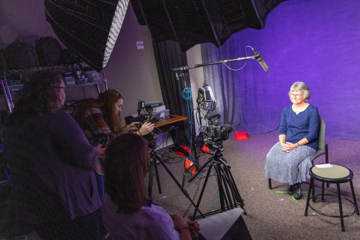 Library employees recording a faculty member in front of a purple backdrop